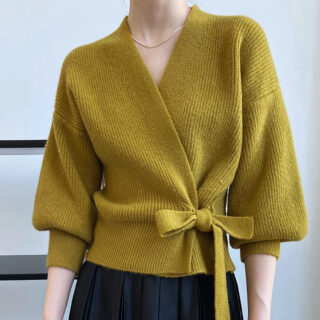 On voit une femme qui porte un gilet cache-cœur jaune avec des manches boules.