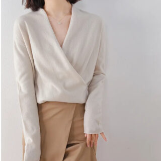 On voit un gilet beige cache-cœur sur une femme brune qui porte aussi une jupe portefeuille camel.