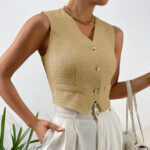 On voit une femme qui porte une gilet de costume beige texture nid d'abeille plutôt court et élégant. Les boutons sont dorés. Elle a un pantalon blanc et porte un sac à main à l'avant bras.