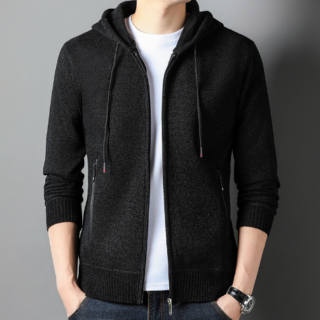 Photo d'un homme debout portant un gilet à capuche foncé zippé ouvert sur un tee-shirt blanc la main droite dans la poche du gilet