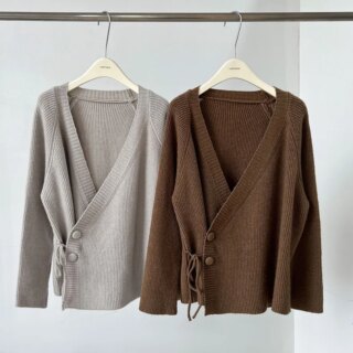 On voit deux gilets cache-cœur, un gris et un marron, qui sont suspendus à une tringle en acier à l'aide de cintres en bois.