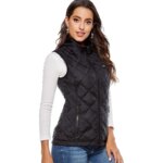 Sur fond blanc, on voit une femme blanche aux cheveux bruns et longs qui porte un gilet chauffant noir, sans manches. Elle a un T-shirt blanc manches longues en dessous et un jean.