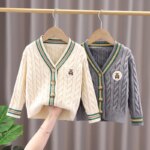On voit deux gilets en laine accrochés à une tringle. L'un est beige, l'autre gris. Il sont devant un rideau taupe.