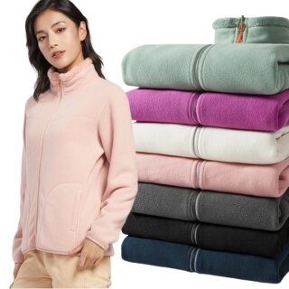 Photo d'une femme portant un gilet polaire et peluche réversible rose avec une pile de gilets pliés de différentes couleurs derrière