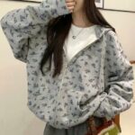 Photo d'une jeune femme aux cheveux longs bruns portant un gilet sweat zippé à capuche gris à imprimé floral sur un tee-shirt blanc
