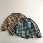 On voit deux gilets pour garçon superposés sur un sol blanc. Le premier est bleu à carreaux beiges, le deuxième marron. Les deux ont un look vintage.