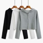 Photo de trois gilets zippés à capuche sur cintres suspendus : un noir, un blanc et un gris