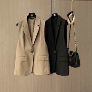 On voit deux gilets de costume pour femmes supendus à une tringle. L'un est noir, l'autre beige. Ils ont une forme de blazer sans les manches.