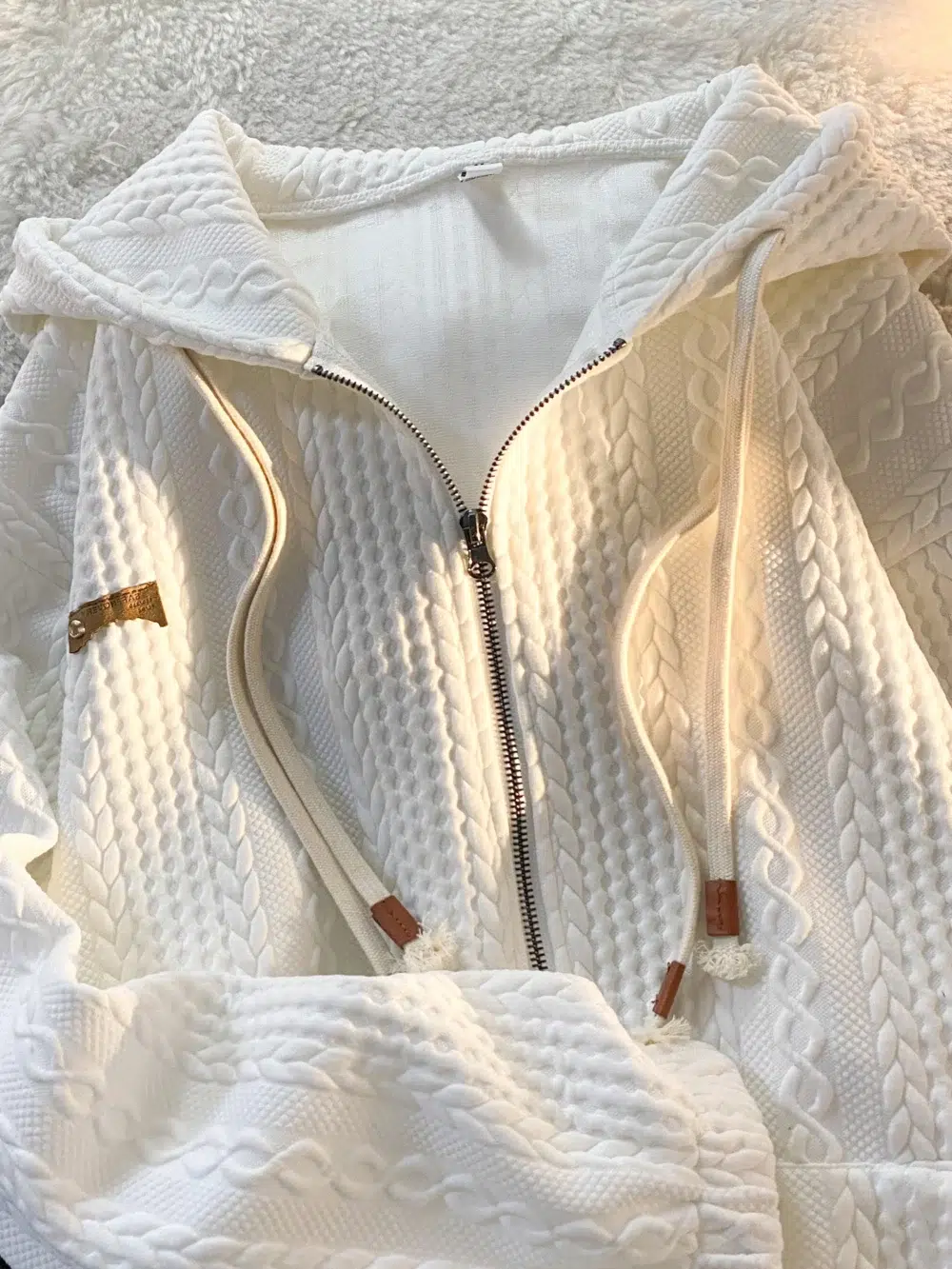 Photo d'un gilet blanc zippé à capuche avec double cordon de serrage et tissu style tricot