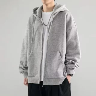 Photo d'un homme portant un gilet sweat gris zippé ouvert à capuche style streetwear large sur un bas noir, un tee-shirt blanc et un collier