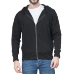 photo d'un homme debout portant un gilet sweat noir zippé à capuche à demi ouvert sur un tee-shirt blanc et un jean