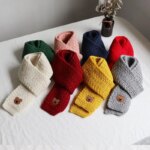 Photo d'écharpe d'hiver pour enfants en grosse maille colorés, pliées avec un petit ourson sur le bout, posées sur une table