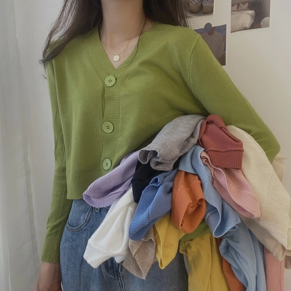 Photo d'une femme portant un gilet court boutonné à col V vert avec pleins de gilet de différentes couleurs sous le bras