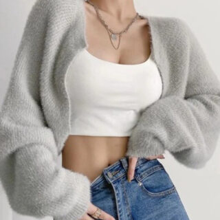 Photo d'une femme portant un gilet court tout doux gris avec de larges manches, par dessu un crop top blanc avec un jean et des colliers