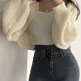 Photo d'une femme portant un gilet court en tricot blanc cassé par dessus un top blanc avec un jean.