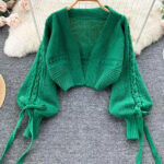 Photo d'un gilet court tricoté vert avec des détails tressés sur les manches posé sur une moquette grise et une peau blache