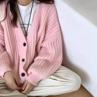 on voit une jeune femme assise en tailleur portant un gilet ample mi-long en tricot rayé de couleur rose