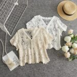on voit sur un sol gris deux gilet aéré court en crochet pour femme un beige et un blanc