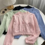 on voit posés sur une table des gilets courts à manches longues en tricot pour femme, il y en a un bleu un rose un vert et un noir