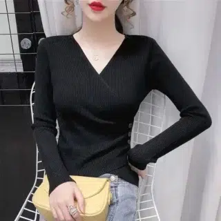 Femme assise de face portant un gilet cache-cœur noir, tenant un sac à main jaune dans sa main droite