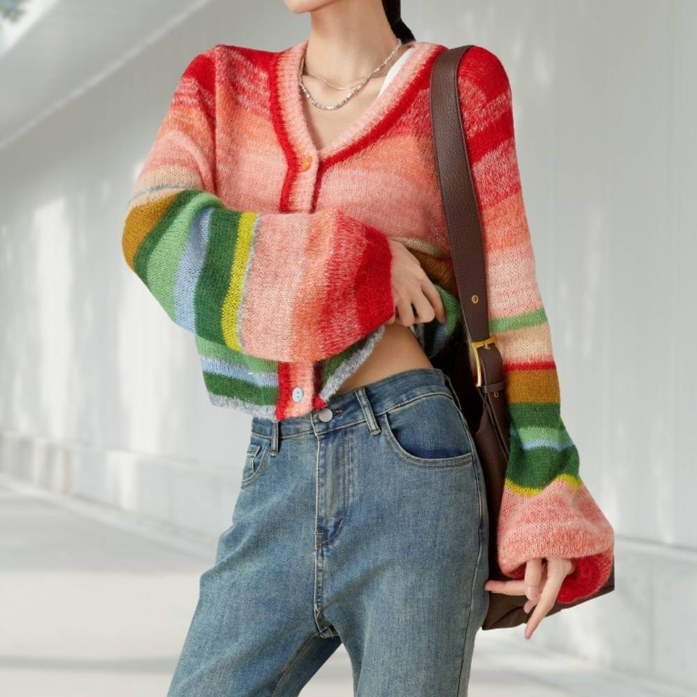 Gilet court tricot coloré style vintage pop Gilet court tricot coloré style vintage pop porté par une jeune femme qui porte également un sac à main sur l'épaule gauche et qui est en avant plan sur un décor de rue.