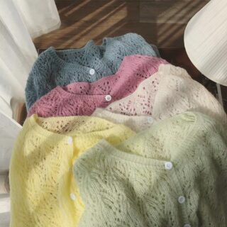 différents gilets en mailles ajourées posés sur une table : bleu, rose, blanc, jaune et vert clair