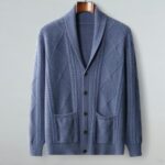 Gilet bleu en maille suspendu à un ceintre sur fond gris